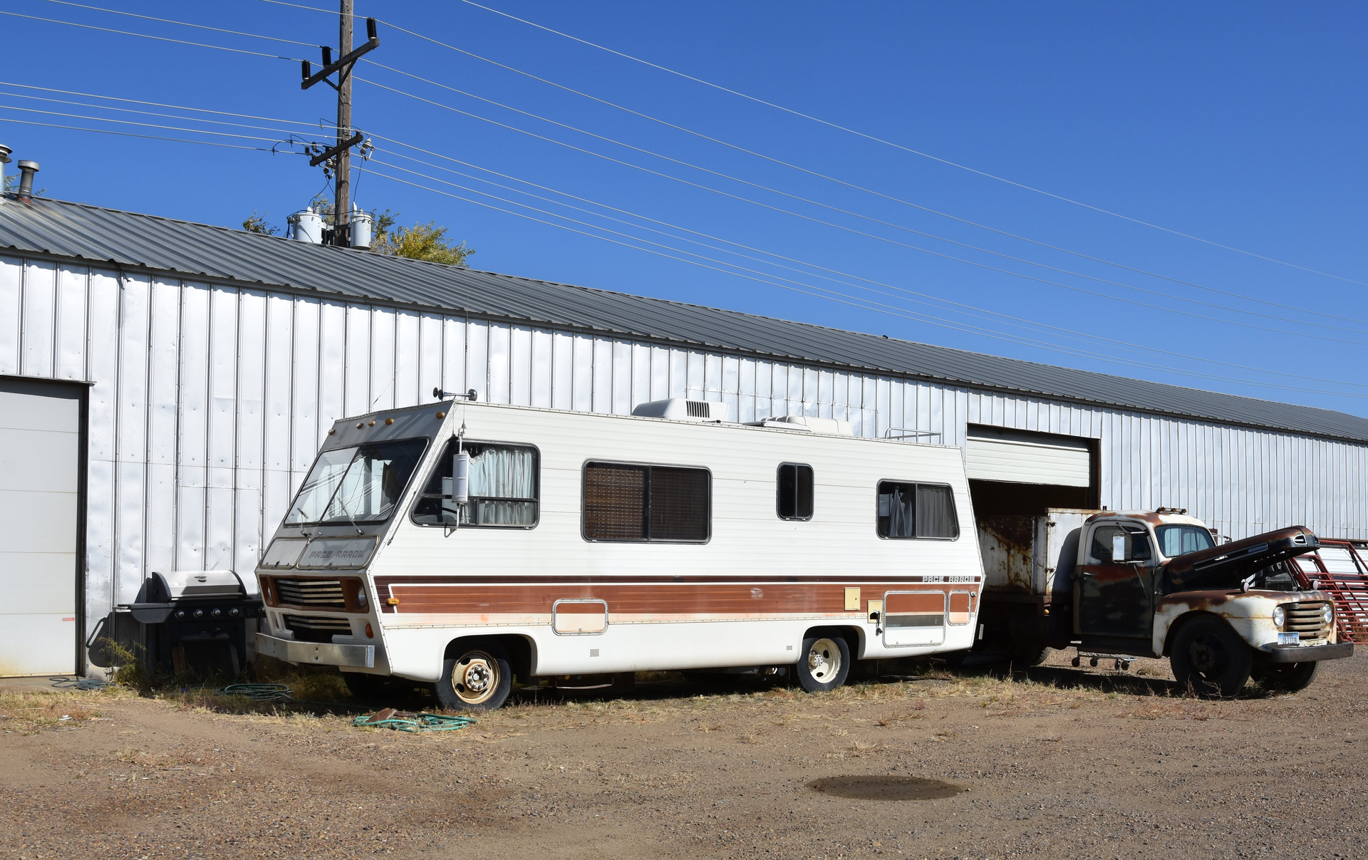 Classic RV parked beside a metal warehouse under a clear blue sky in Glasgow, Montana. Perfect for travel and lifestyle themes.
